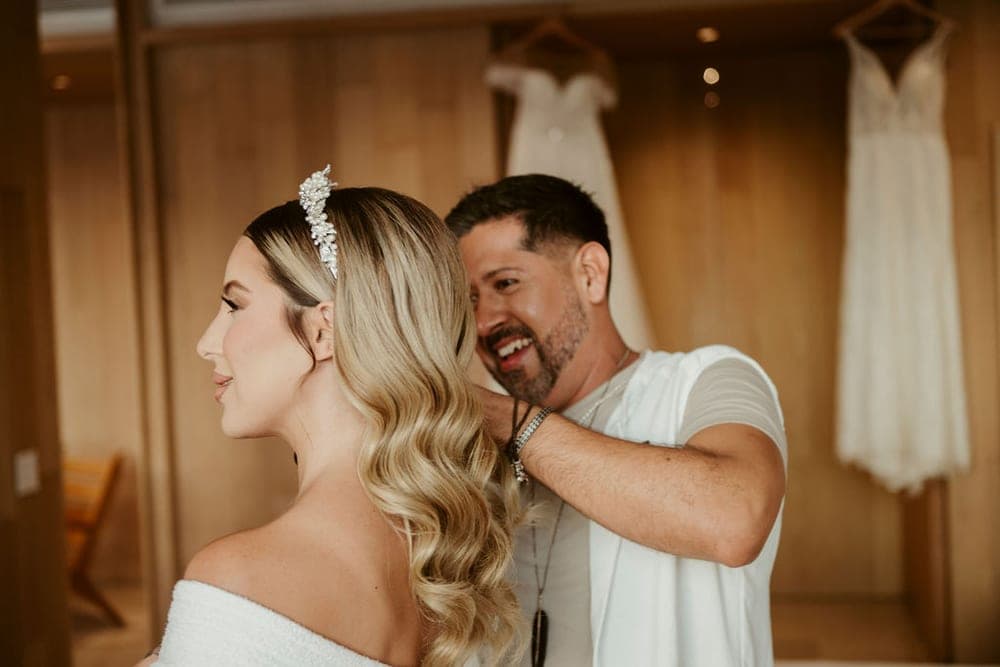 Artista de Mich & Beauty acomodando las ondas de la novia junto a los vestidos colgados